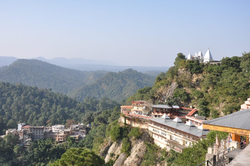 A panoramic view of Baba Balak Nath Temple perched on a hilltop with lush green mountains in the background.