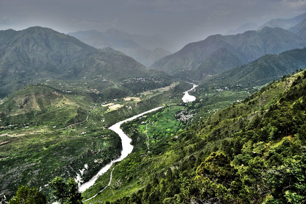 A panoramic view of the Satluj River winding through lush green valleys and surrounded by majestic mountains in Himachal Pradesh.